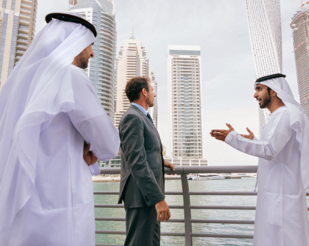 Business discussion with professionals in traditional Emirati attire against a modern UAE city skyline, representing achievements in UAE business and technology.